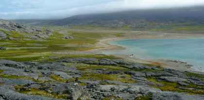 Rocky and grassy hills with turquoise bay and low clouds